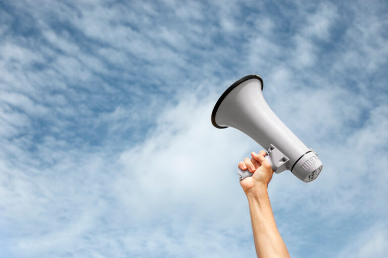 hand holds megaphone in the air against cloudy sky